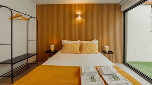 Habitación de hotel con cama, pared de paneles de madera, ventana con vistas y un perchero.