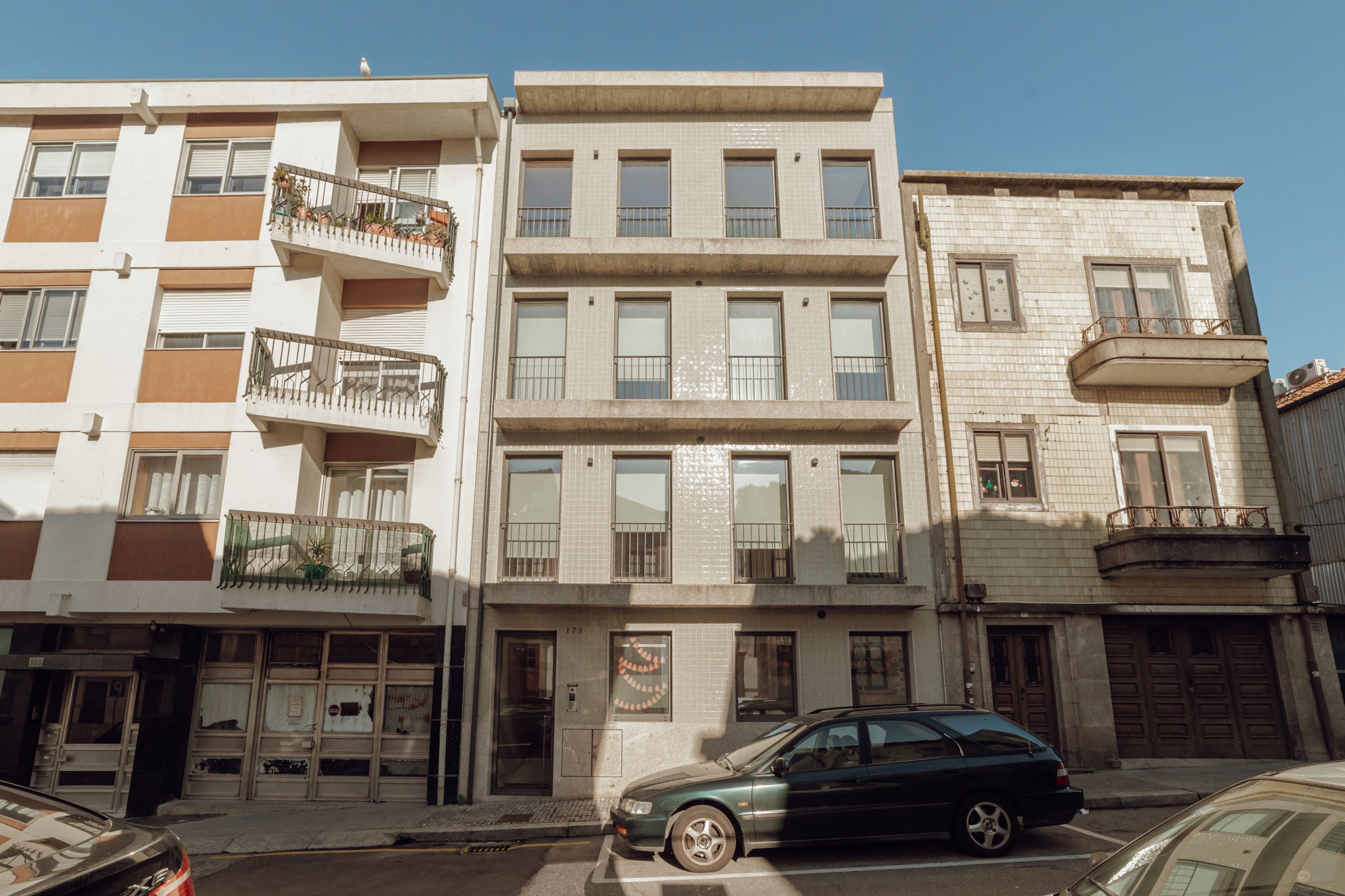 Um edifício de vários andares com varandas, um carro estacionado na frente e um céu azul límpido.