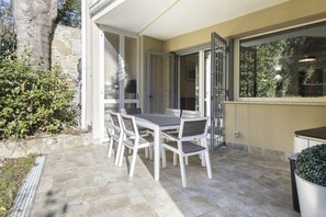 Een terras buiten met een tafel en stoelen, een stenen muur en een groot raam.