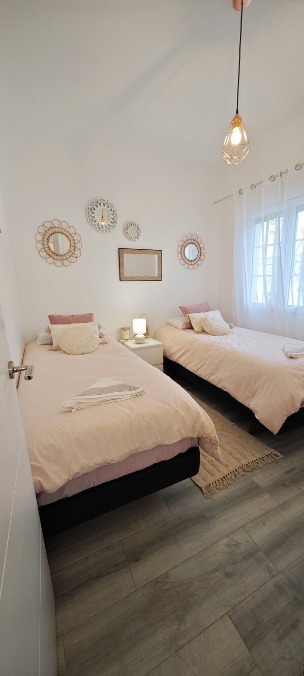 A bedroom with two beds, a bedside table with a lamp, decorative wall mirrors, and a window with curtains.