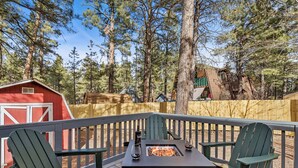 A deck with Adirondack chairs, a fire pit, and a red building in the background.