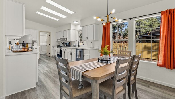 A modern kitchen with white cabinets, a wooden dining table, and a hanging light fixture.