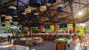 An outdoor bar area with wooden furniture, a pool table, and hanging lights.