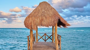 A wooden pier leading to a thatched-roof structure over water.
