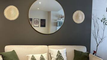 A neutral-toned sofa with a woven throw blanket, two round wall decorations, and a round mirror.