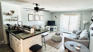 A modern kitchen with a central island, a dining area with a round table, a sofa, and a ceiling fan. - A Perfect Mountain Getaway with Hot Tubs, and steps to Soaring Eagle ski lift! (Snowshoe)