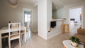 A modern living room with a white dining table, a TV on a stand, a wooden stool, and a sofa. - 2BR Penthouse in downtown with sunny terrace (Sevilla)