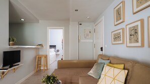 A modern living room with a sofa, a coffee table with a plant, a TV on a stand, and artwork on the walls. - 2BR Penthouse in downtown with sunny terrace (Sevilla)
