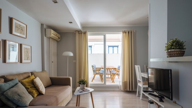 A living room with a sofa, a small table with a plant, a TV, and a balcony with a table and chairs. - 2BR Penthouse in downtown with sunny terrace (Sevilla)