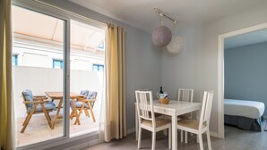 A dining area with a white table and chairs, a glass door leading outside, and a bed in the adjacent room. - 2BR Penthouse in downtown with sunny terrace (Sevilla)