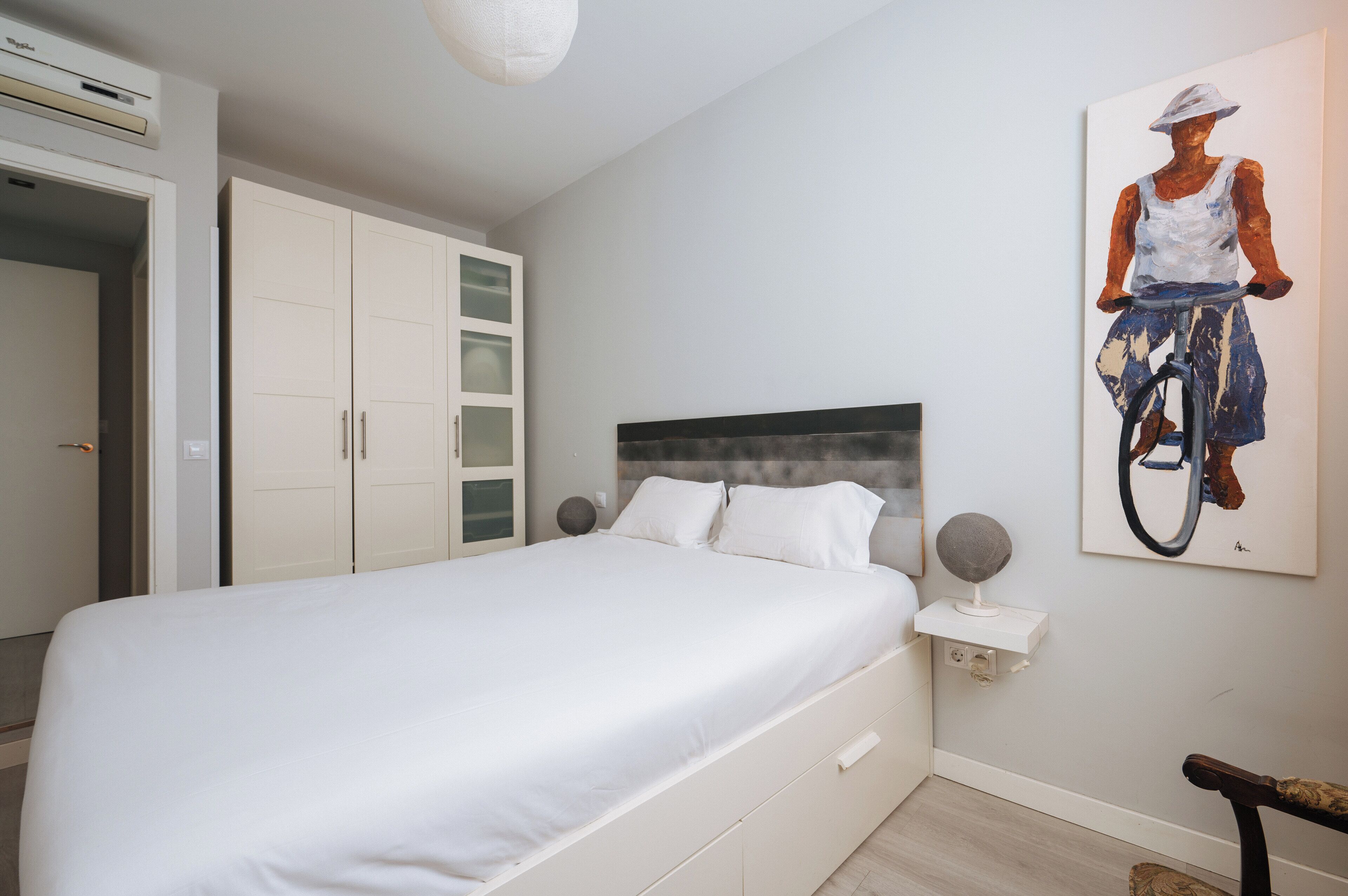 A bedroom with a large bed, white wardrobe, and a painting on the wall.