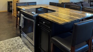Una cucina moderna con isola centrale, sedie nere, illuminazione a sospensione e un'ampia finestra.