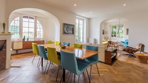 Un'ampia stanza con un grande tavolo da pranzo in legno circondato da sedie colorate, un caminetto e un'accogliente area relax con un divano blu e una poltrona in pelle.