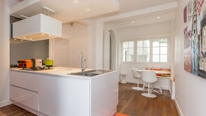 Una cucina moderna con isola centrale, mobili bianchi e piano cottura integrato. C'è un'area pranzo con tavolo e sedie bianche, e un tappeto colorato sul pavimento.