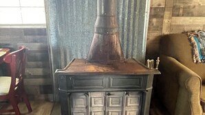 A wood-burning stove with a metal chimney, a cushioned bench, and a wooden floor. - Terrific 1-bedroom off grid cabin in Belfry with Mountain View (Belfry)