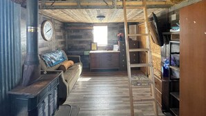 A rustic cabin interior with a wooden ceiling, a fireplace, a couch, a ladder, and a wooden bookshelf. - Terrific 1-bedroom off grid cabin in Belfry with Mountain View (Belfry)