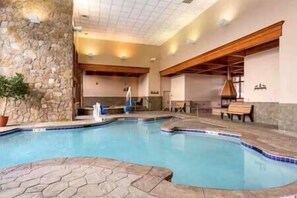 A swimming pool with stone walls and wooden beams, surrounded by a patio area with seating. - Grand Timber Concierge Resort  Ski-In/Out, sleeps 8
ONLY Feb 21 - Mar 07, 2026 (Breckenridge)