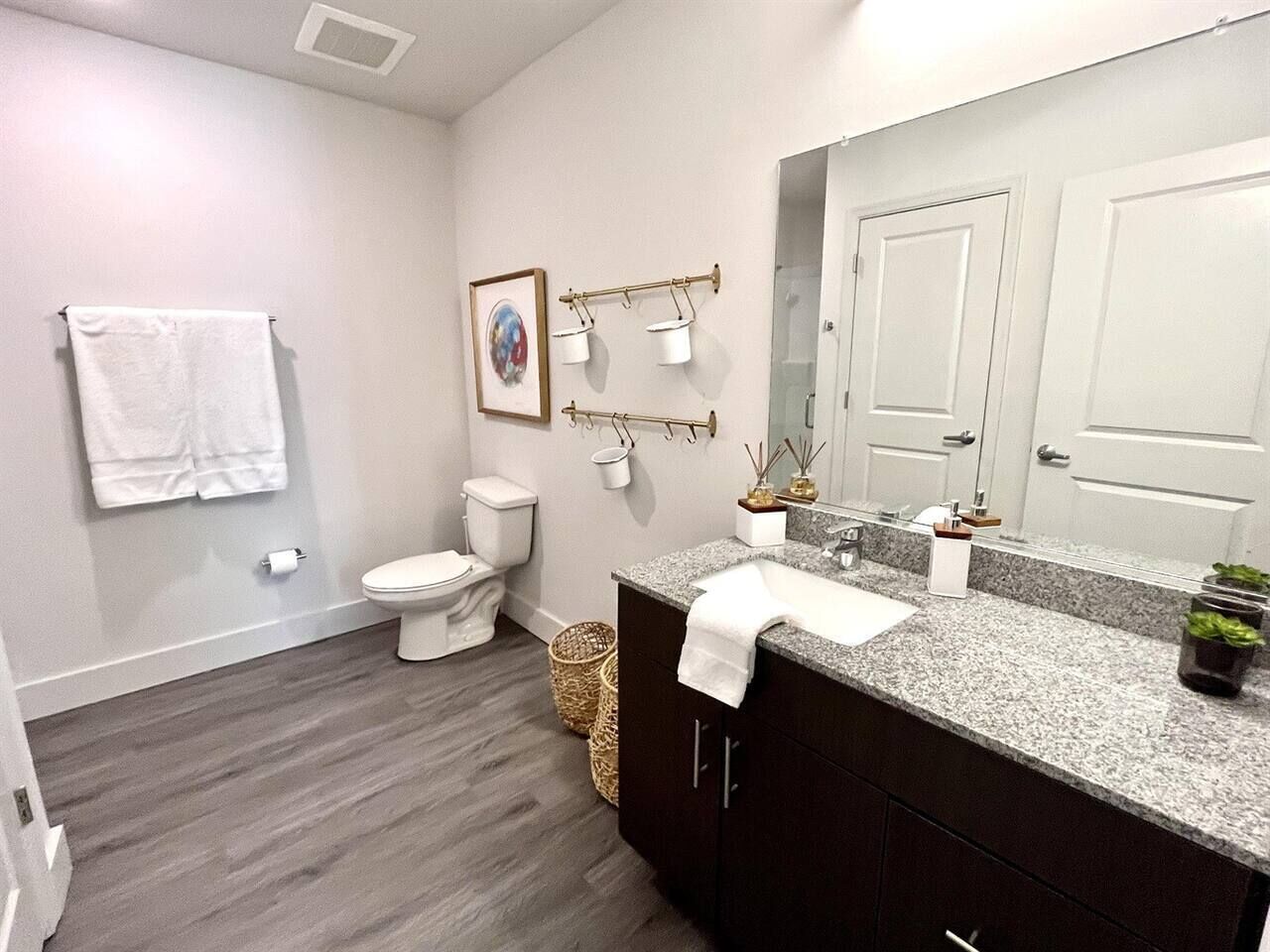 Ein modernes Badezimmer mit Toilette, Waschbecken und Spiegel. Handtücher hängen an der Wand und ein Korb steht auf dem Boden.