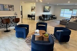 Un salon moderne avec une cheminée, des fauteuils bleus, une table basse et un coin repas équipé d’un téléviseur.