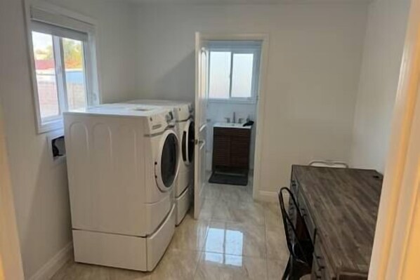 Une buanderie équipée d’un lave-linge et d’un sèche-linge, d’un petit évier et d’une porte donnant sur une autre pièce.