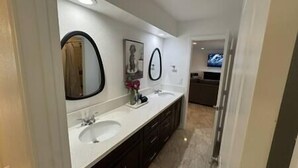 Un baño moderno con dos lavamanos, un espejo grande y una ventana pequeña.