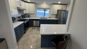 Cocina compacta con gabinetes blancos, un refrigerador de acero inoxidable y un microondas.