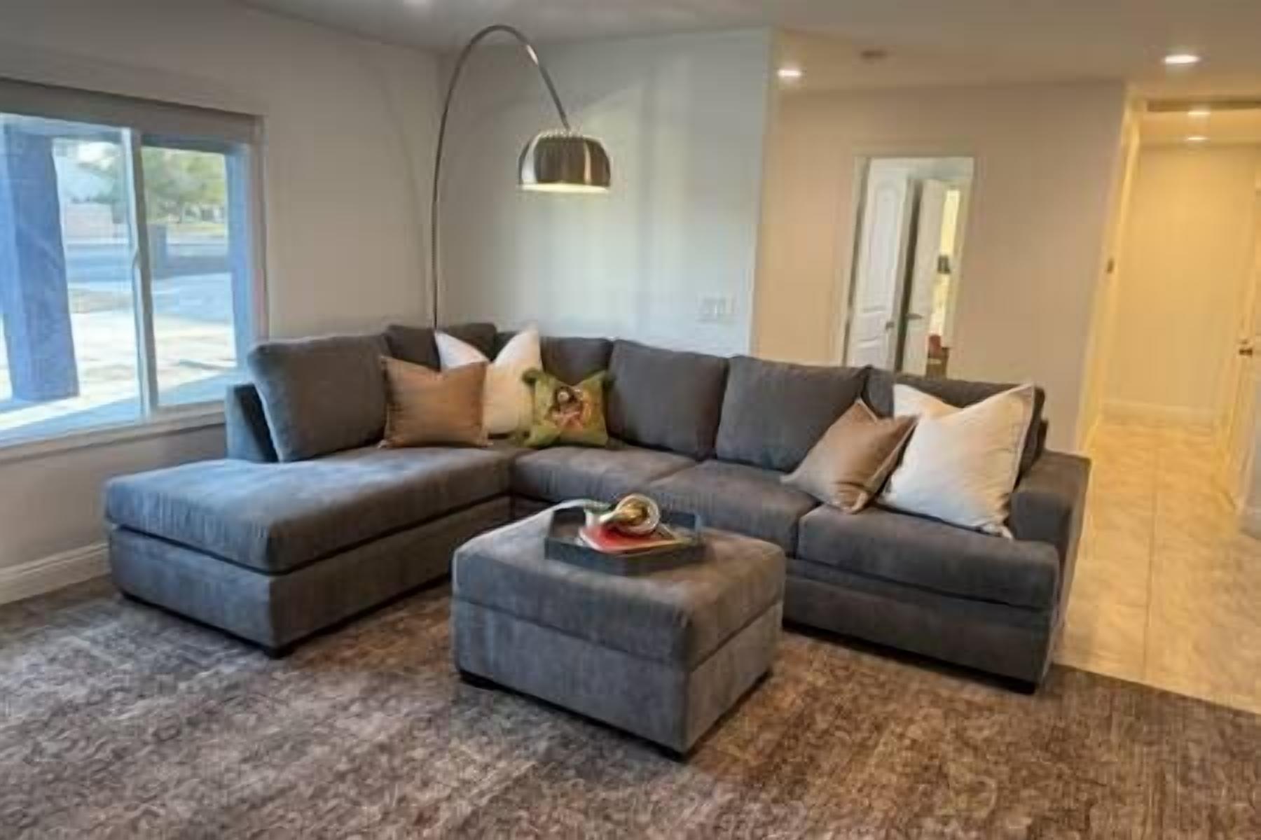 A modern living room with a sectional sofa, a coffee table, and a large window providing natural light.