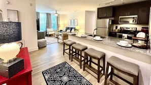 A modern kitchen with a central island, bar stools, and a dining area with a sofa and chairs. - The Spot that Ever Calls - Walk to OM & Square! (Oxford)