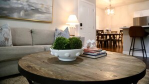 A cozy living room with a round wooden coffee table, a white bowl with green moss, and a bookshelf with books.