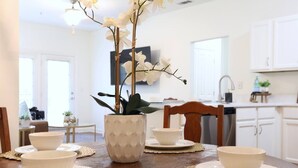 Une table à manger dressée avec des bols et des assiettes blancs, un vase décoratif contenant des fleurs blanches et une chaise en bois.