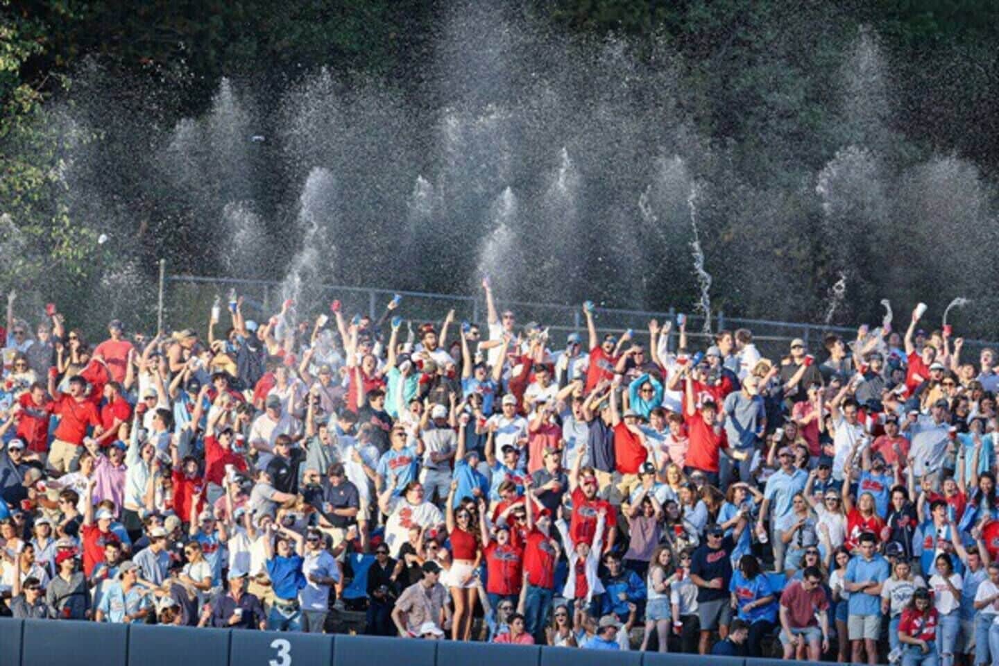 A crowded outdoor event with people standing and cheering, and water being sprayed in the air.