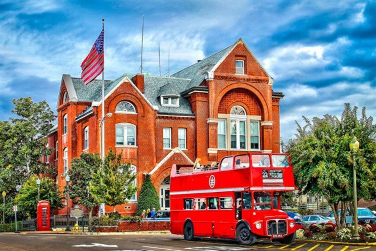 A red double-decker bus in front of a large brick building with a flag.
