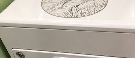 A white washing machine with a leaf pattern on the top, a control panel with knobs, and a front handle.