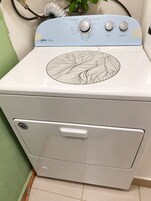 Una lavadora blanca con un estampado de hojas en la parte superior, un panel de control con perillas y un frente con asa.