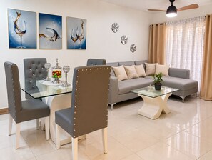 A modern living room with a glass coffee table, leather chairs, a grey sofa, and decorative wall art. - Comodidad, seguridad y cercano a todo (Santo Domingo Este)