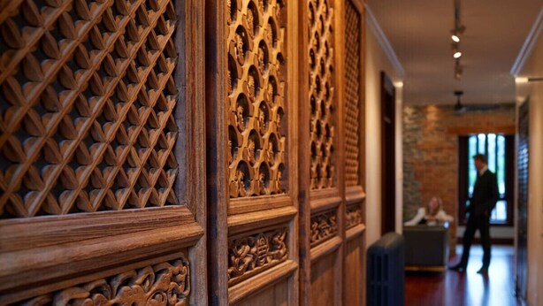 A corridor with intricate wooden paneling and a person walking in the background. - The Madder Suite at Blue Violin (Belleville)