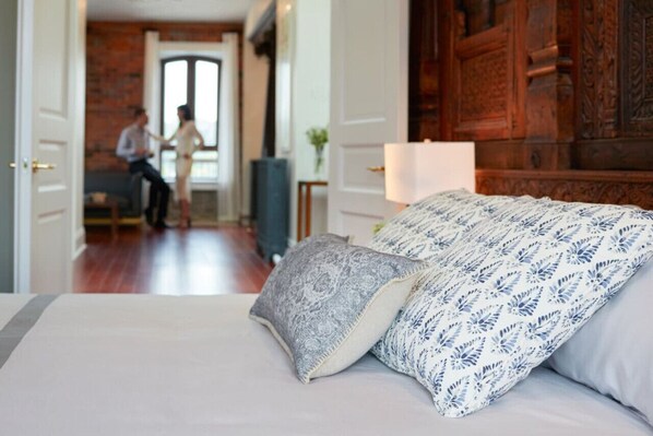 Habitación de hotel con cama, cabecera de madera y una pareja al fondo.