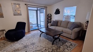 Ein geräumiges Wohnzimmer mit großem Teppich, einer Couch, einem Sessel und einem Couchtisch.