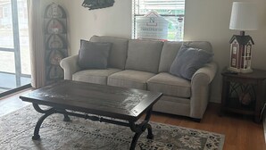 Ein Wohnzimmer mit einer Couch, einem Couchtisch, einem gemusterten Teppich, einer Lampe und einem Fenster mit Jalousien.