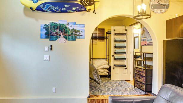 A room with a bunk bed, a small seating area, and a hallway leading to a bathroom. - Electric Fireplace: Central Coeur d'Alene Studio! (Coeur d'Alene)