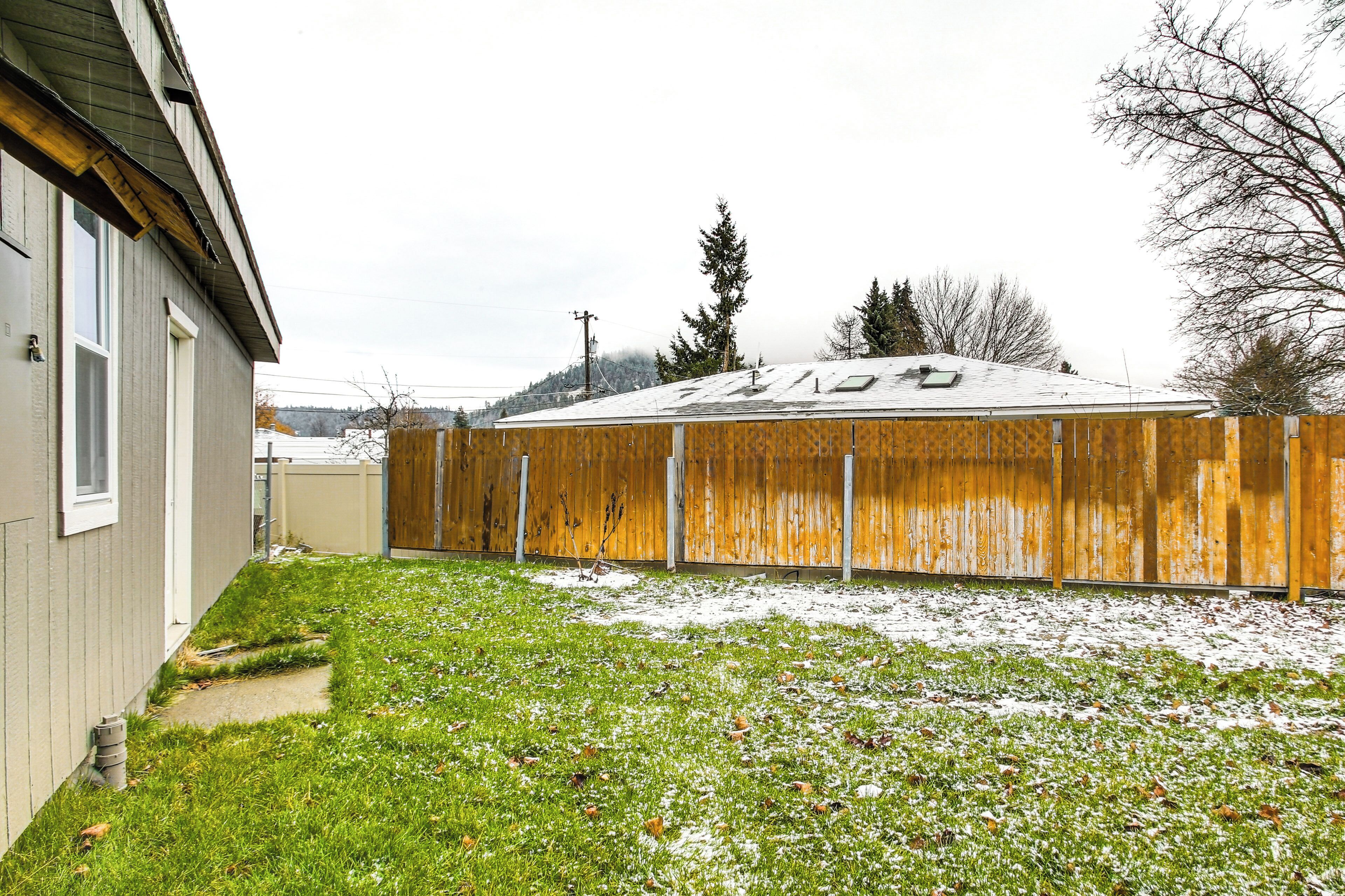 A fenced backyard with a wooden fence, a grassy area, and a house with a visible window and door.