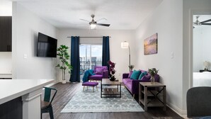 Ein modernes Wohnzimmer mit einem violetten Sofa, einem Couchtisch und einem an der Wand befestigten Fernseher.