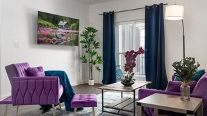 Ein modernes Wohnzimmer mit einem violetten Sofa, einem Couchtisch und einem großen Fenster mit blauen Vorhängen.