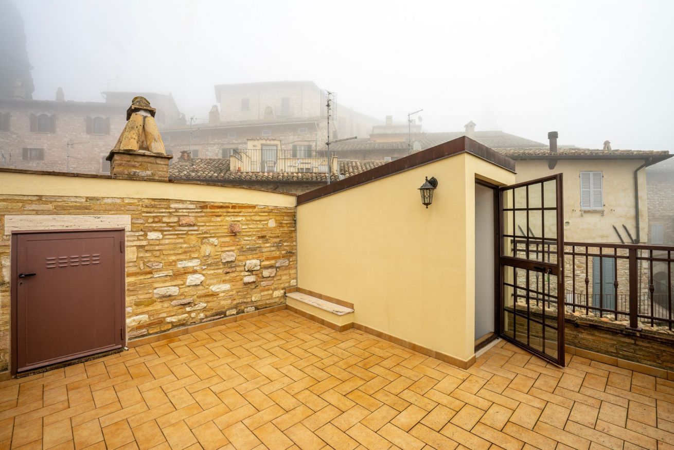 Une terrasse sur le toit, avec un mur en pierre, une porte marron et une porte vitrée donnant sur un balcon.