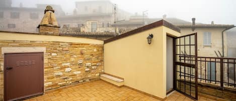 A rooftop terrace with a stone wall, a brown door, and a glass door leading to a balcony.