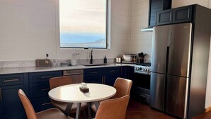 A modern kitchen with a round dining table, two chairs, a refrigerator, and a stove. - Earhart Cabin at Ever Sky Ranch (Shell)