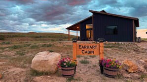 A cabin named Earhart Cabin with a wooden sign, two flower pots, and a view of the surrounding landscape. - Earhart Cabin at Ever Sky Ranch (Shell)