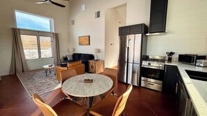 Een moderne keuken met een centraal eiland, roestvrijstalen apparatuur en een eethoek met een ronde tafel en stoelen.