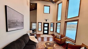 A spacious living room with a large window, a mounted deer head, and a framed historical photograph on the wall.