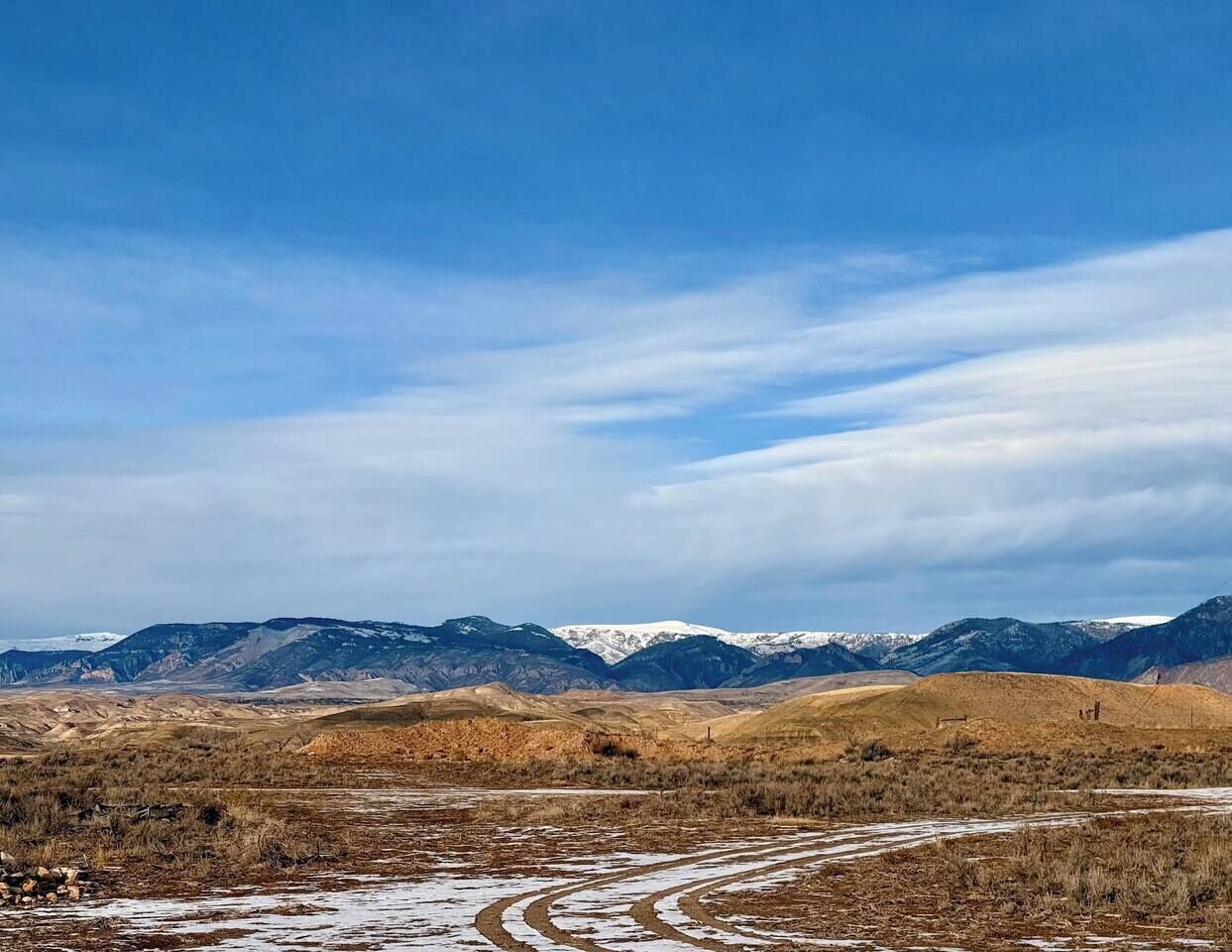 Un vaste paysage de collines douces et de montagnes lointaines, sous un ciel dégagé.